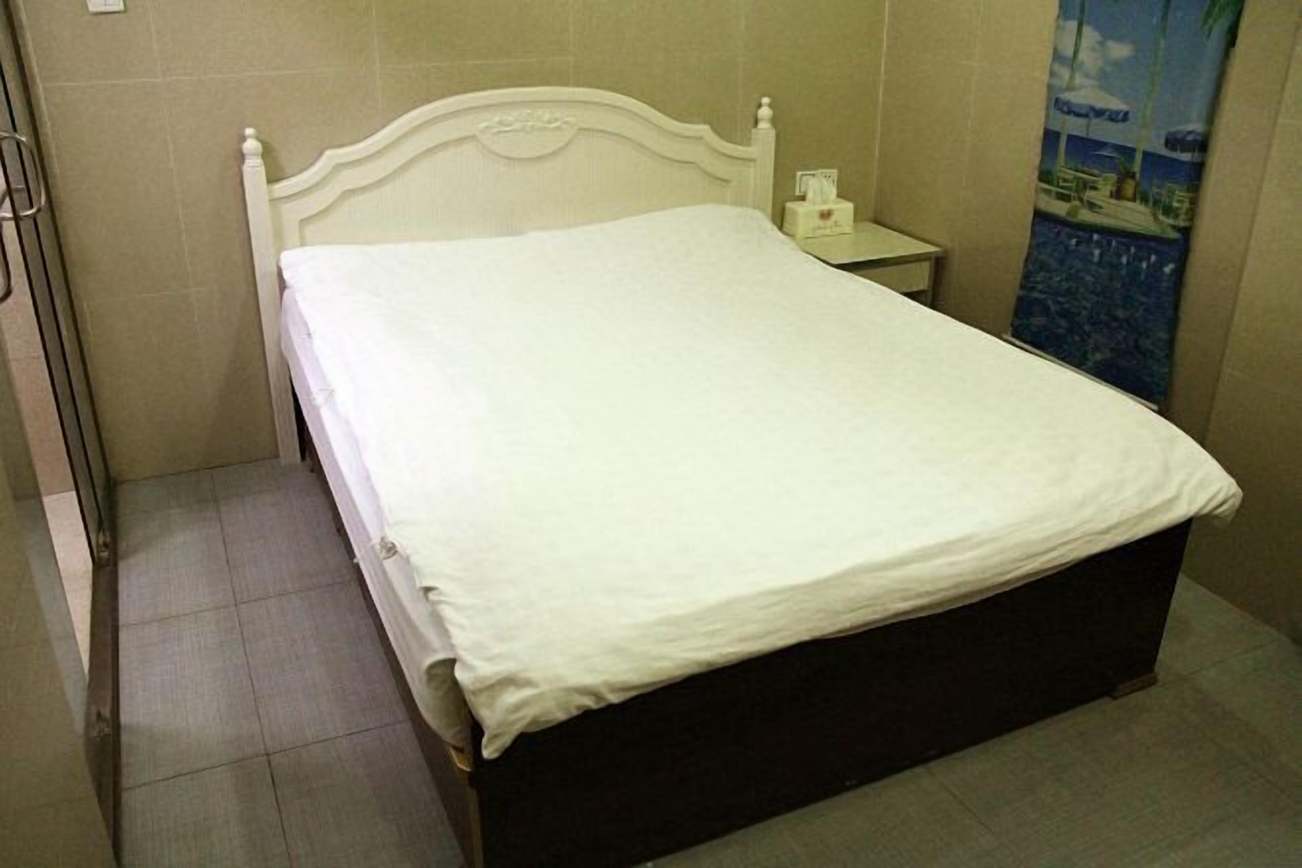 A single bed with a white headboard and footboard, a bedside table with a lamp, and a poster on the wall.