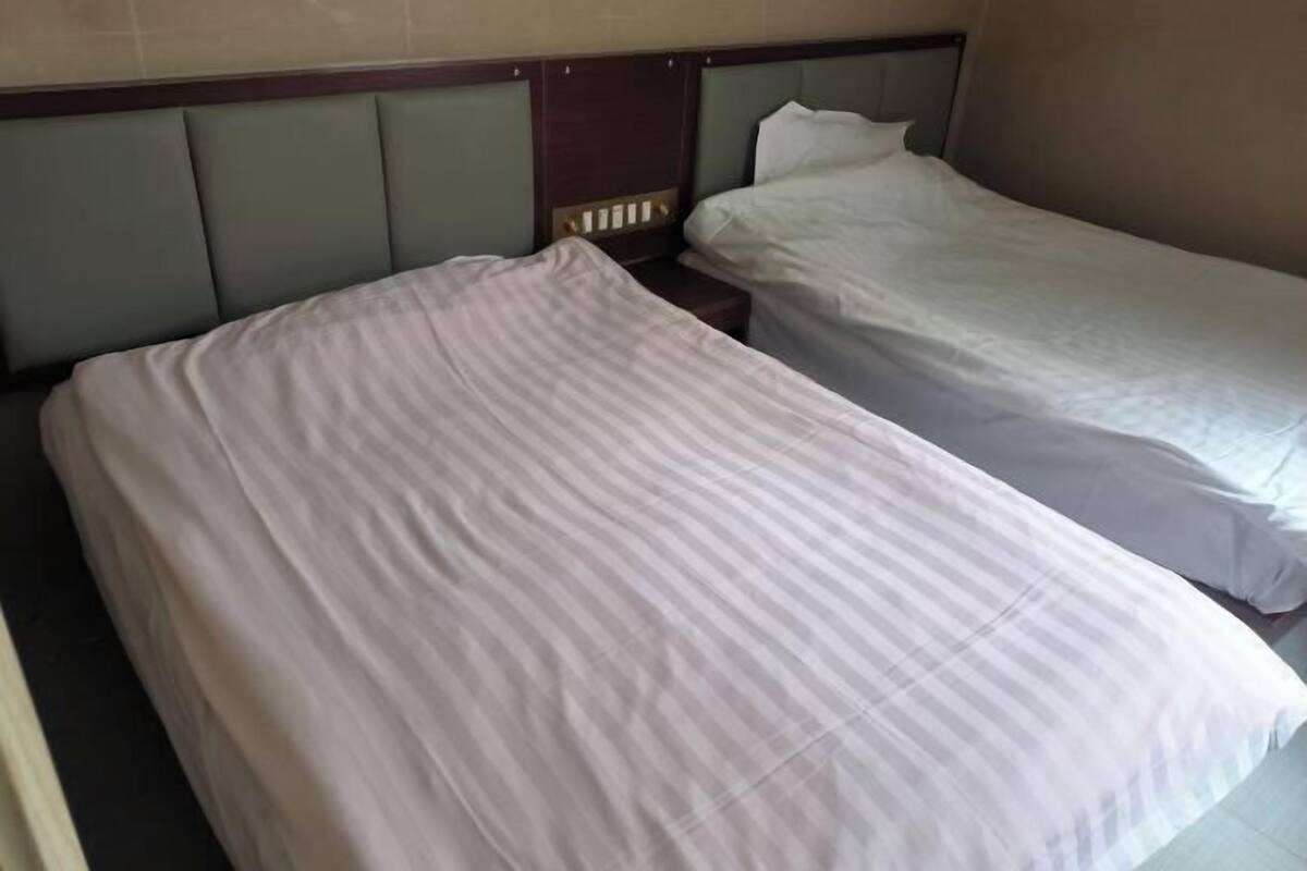 Une chambre d’hôtel avec deux lits simples, une tête de lit en bois et un mur sobre.