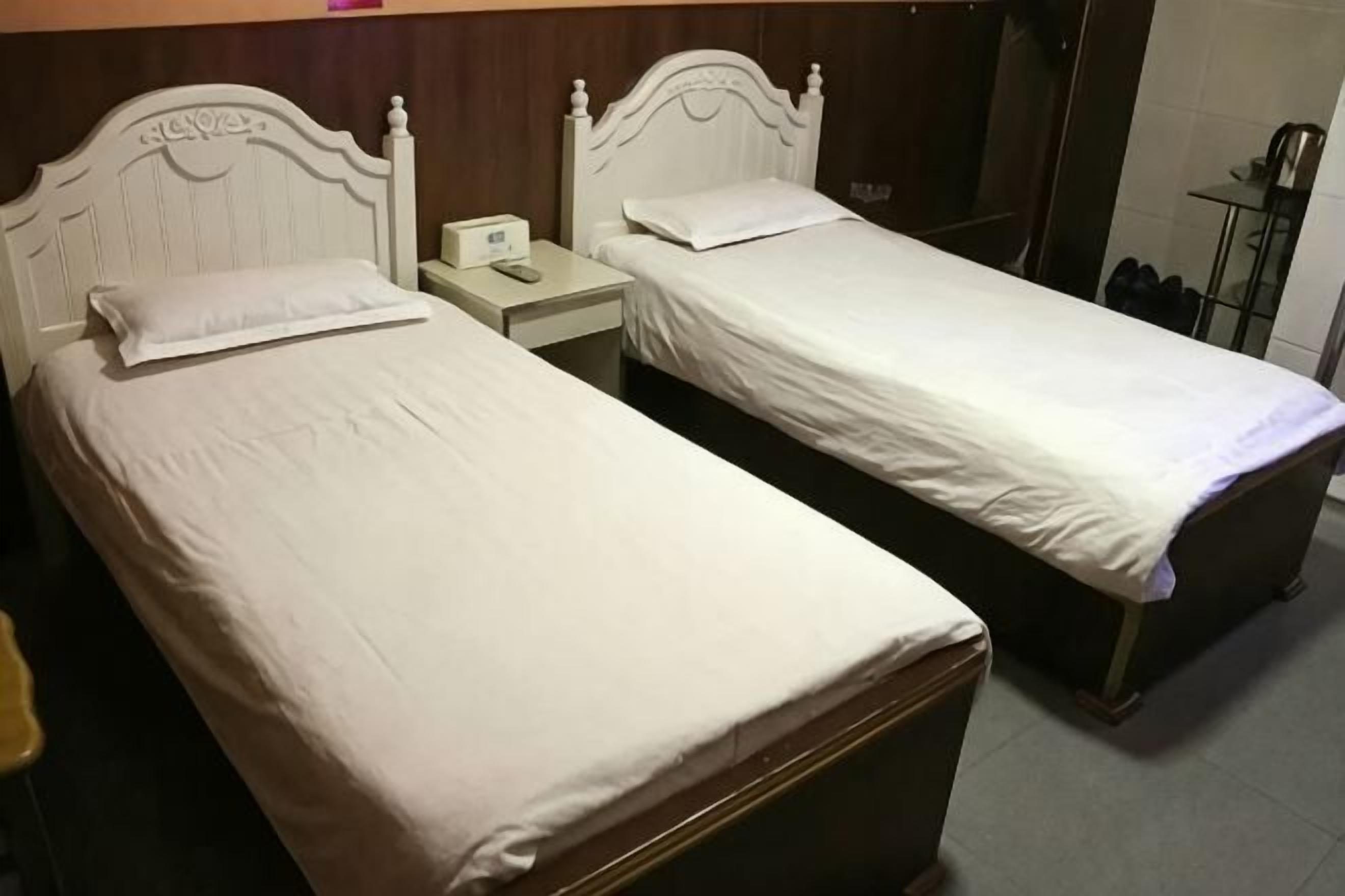 Dos camas individuales con cabeceros de madera, una mesita de noche con un teléfono y un espejo en la pared.