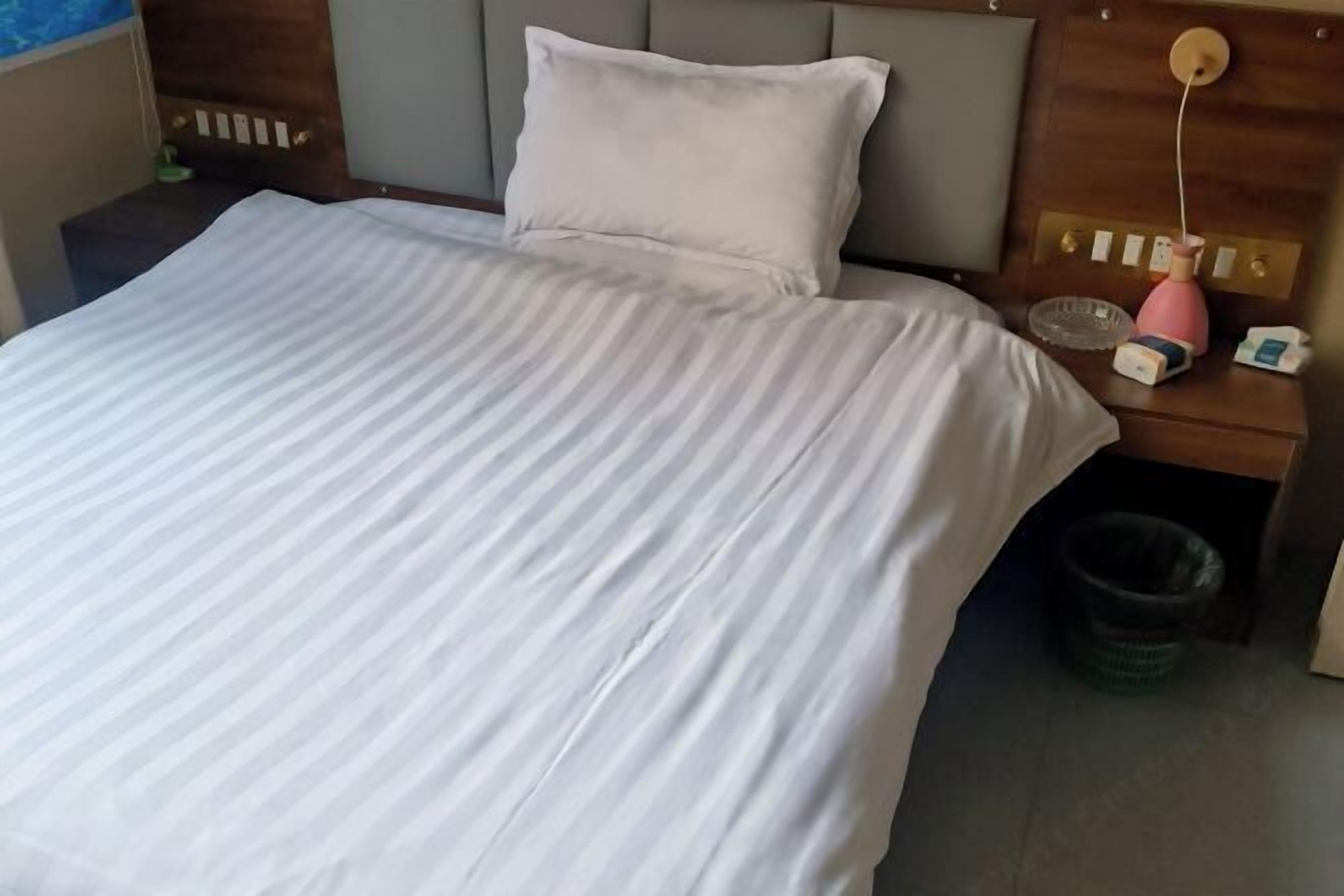 A hotel room with a bed, a nightstand, a lamp, and a trash bin.