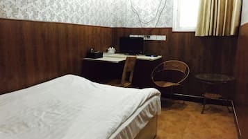 Una habitación con cama, escritorio con silla, una mesita y ventana con cortinas.
