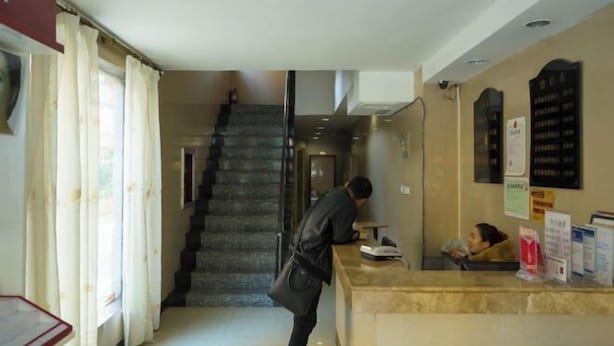 Ένας χώρος υποδοχής ξενοδοχείου με έναν μαρμάρινο πάγκο, μια σκάλα στο βάθος και μια γυναίκα καθισμένη στον πάγκο.