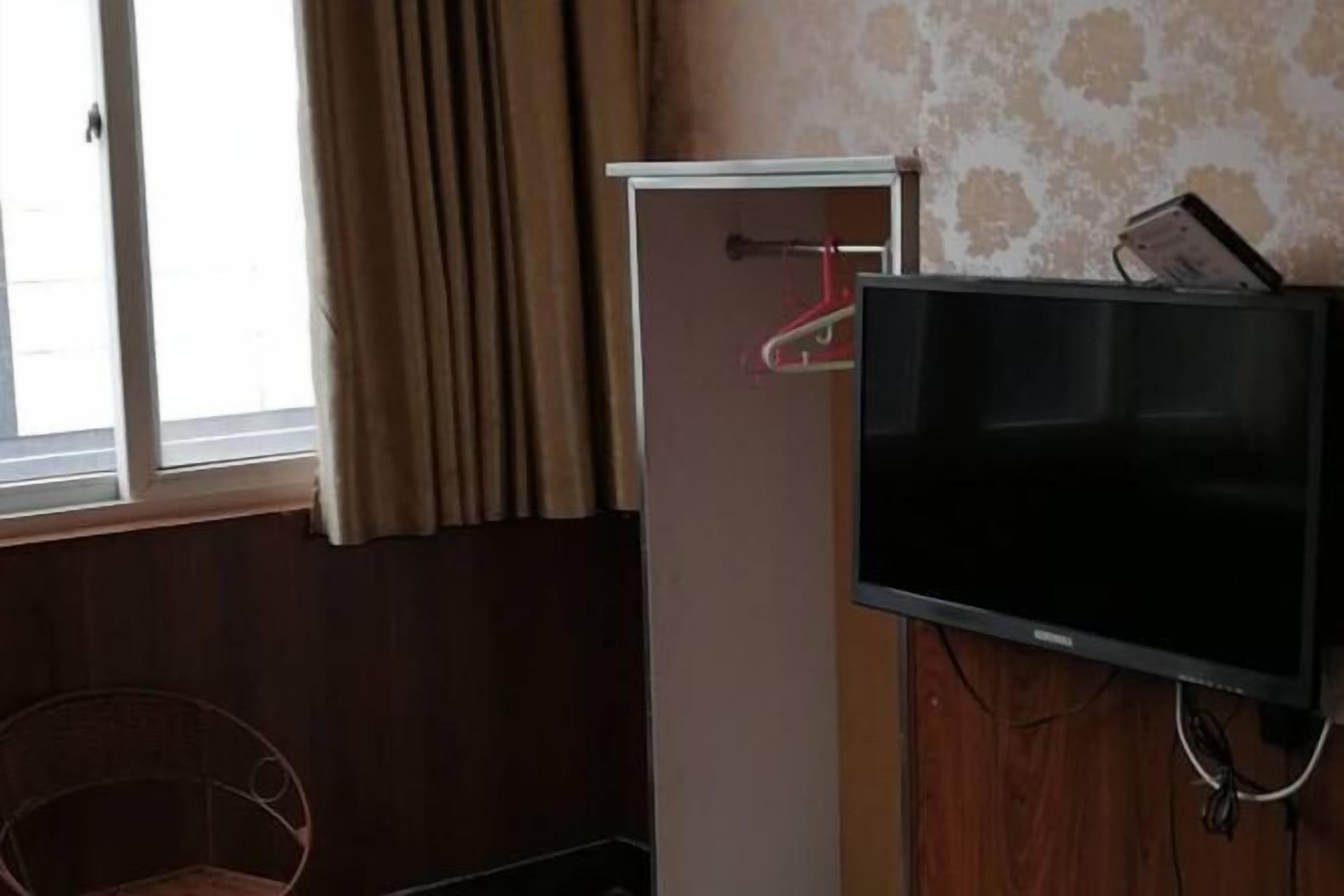 A room with a television mounted on the wall, a window with curtains, and a coat rack with a red hanger.