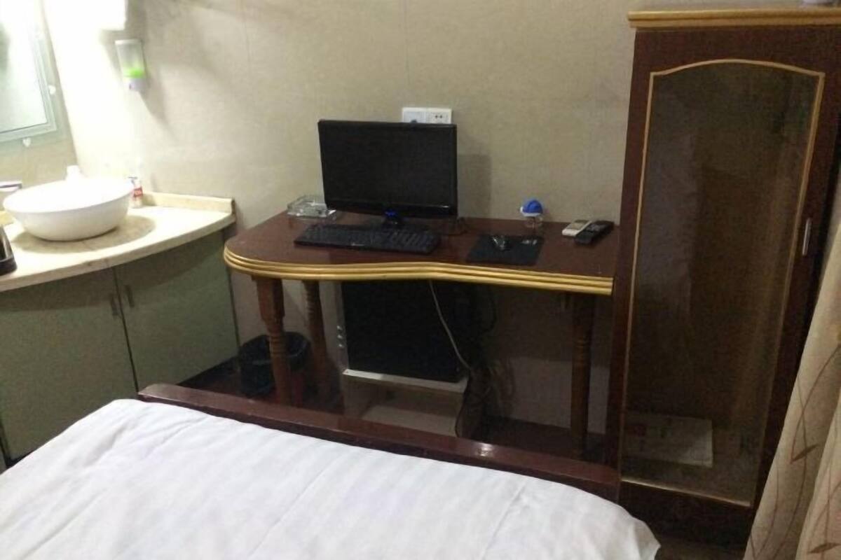 Une chambre d’hôtel comprenant un lit, un bureau avec un ordinateur, un petit lavabo et une armoire.