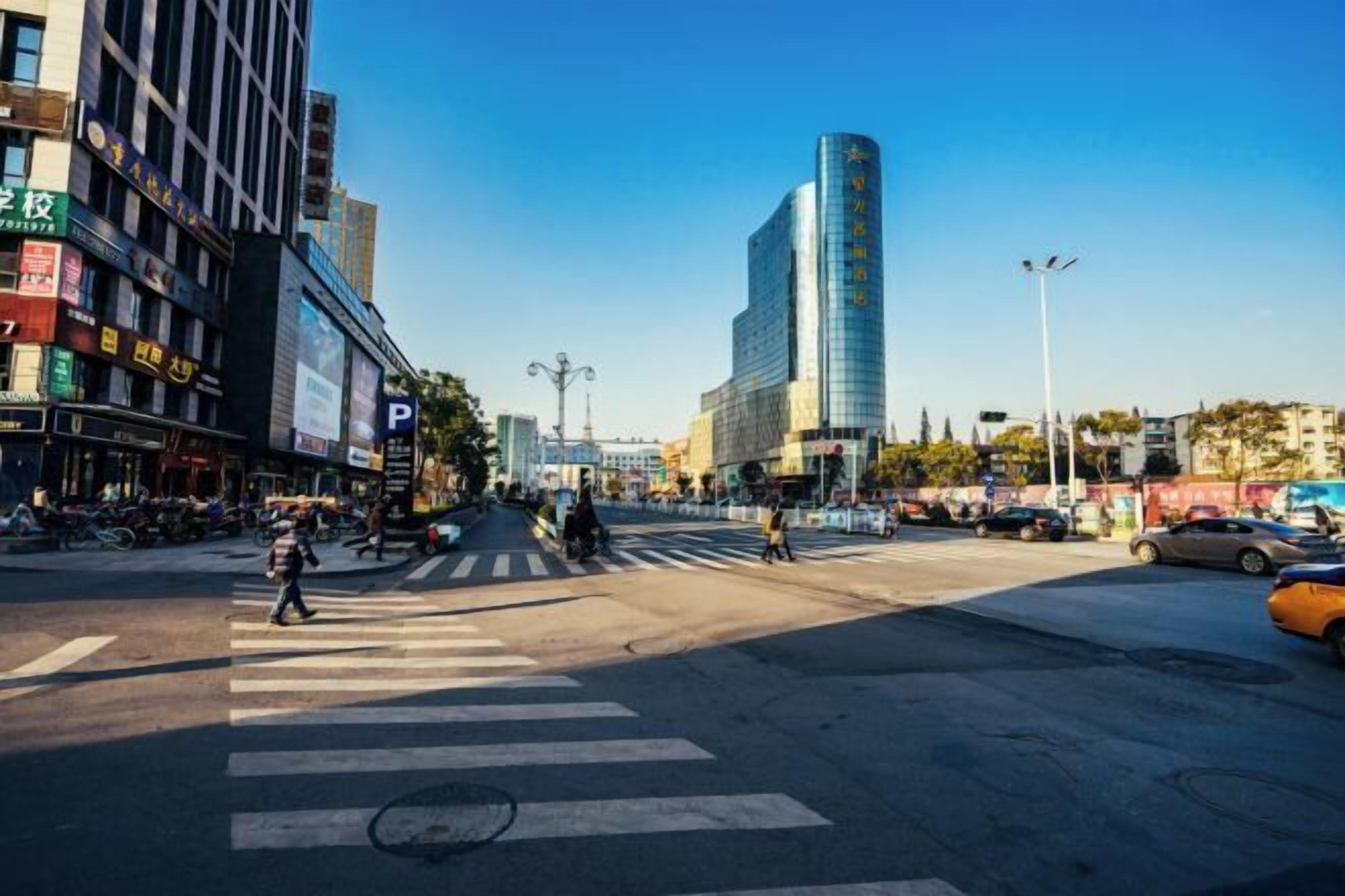 A busy urban street with a pedestrian crossing, tall buildings, and a clear blue sky.