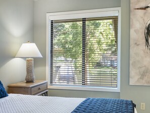 A bedroom with a bed, a nightstand, a lamp, and a window with blinds.