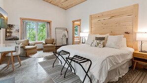 Ein geräumiges Schlafzimmer mit einem großen Bett, einem Schreibtisch und einem Sessel, mit Holzboden und großen Fenstern.