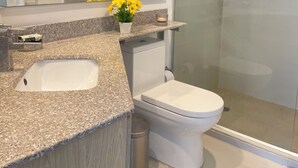 A modern bathroom with a granite countertop, a white sink, a toilet, and a glass shower enclosure.