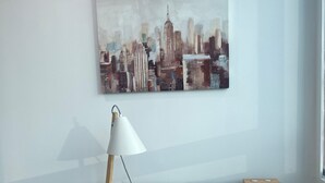 A modern workspace with a wooden desk, a white chair, a lamp, and a cityscape painting on the wall.