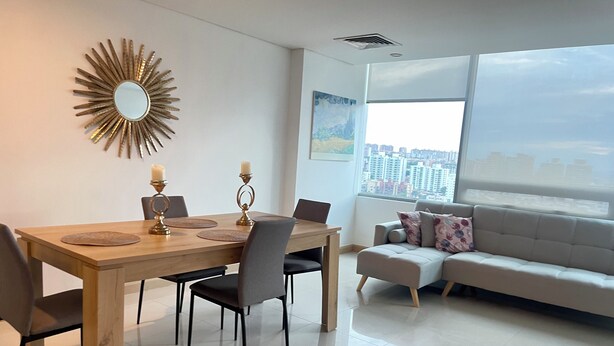 A modern living room with a dining table, chairs, a sofa, and a large window with a city view.