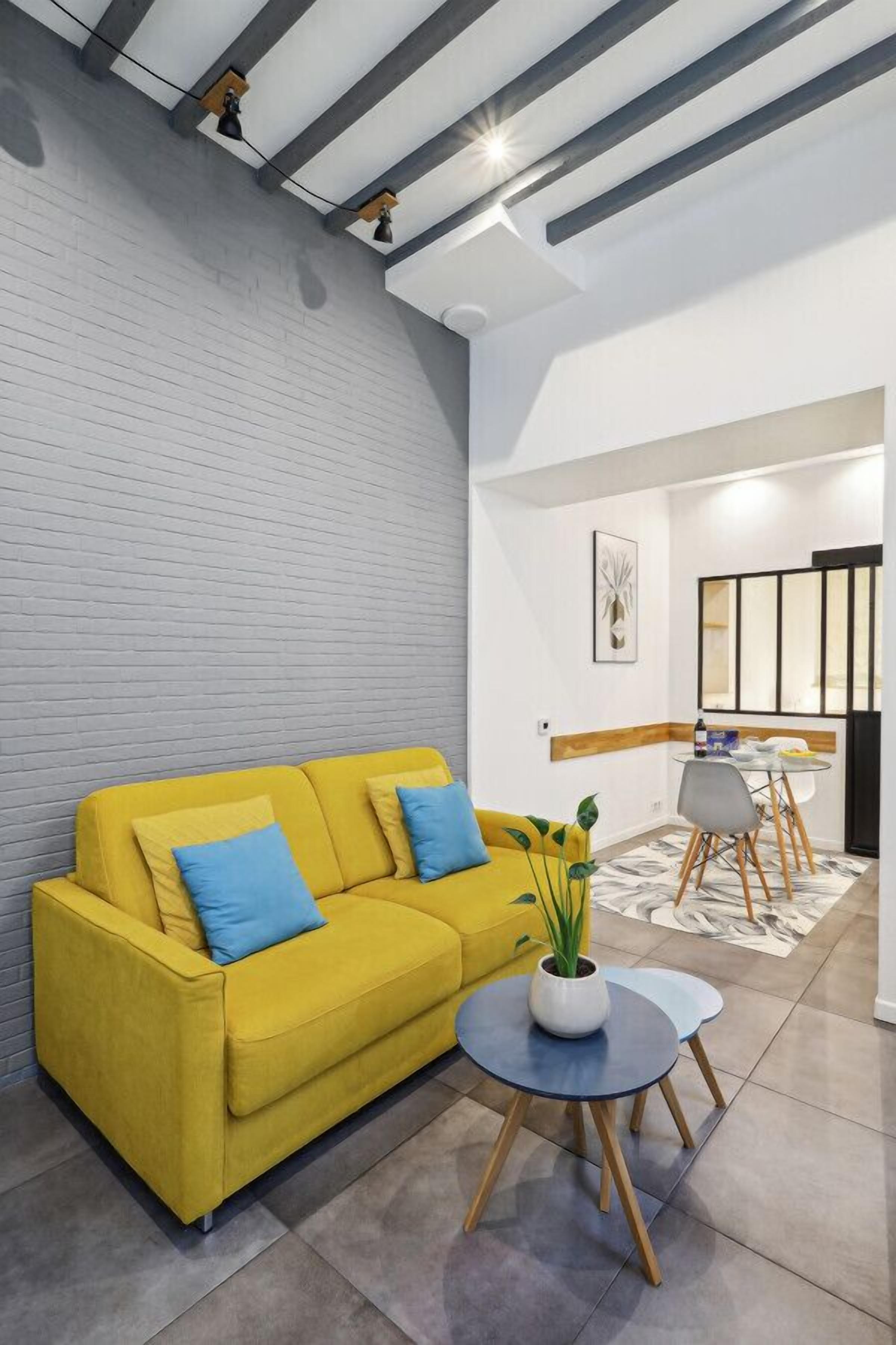 A modern living room with a yellow sofa, a small round table, and a potted plant.