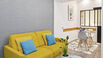A modern living room with a yellow sofa, a small round table, and a potted plant.