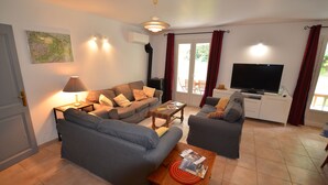 Una sala de estar con un sofá, una mesa de centro, un televisor y un ventanal corredero al exterior.