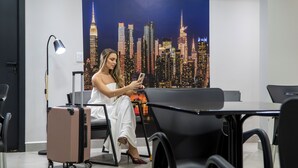 A room with a cityscape view, a desk, a chair, a lamp, and a suitcase. - TNY APART BARRETOS (Barretos)