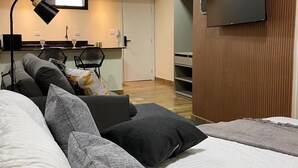 Ein modernes Hotelzimmer mit einem großen Bett, einem Schreibtisch mit Stuhl, einem wandmontierten Flachbildfernseher und einer Küchenzeile.