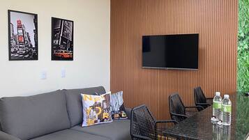Una sala de estar moderna con un sofá gris, sillas negras, un revestimiento de pared de madera, un televisor de pantalla plana y dos carteles enmarcados con vistas a la ciudad.