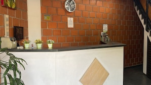 A reception area with a brick wall, a clock, a reception desk, and a staircase. - Hotel Linda (Salto)