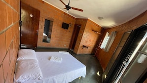A hotel room with a bed, a ceiling fan, a brick wall, a door, and a window. - Hotel Linda (Salto)