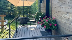 A wooden deck with a table and chairs, a large umbrella, and potted plants. - Brand New, Luxury 1-bedroom apartment with AC, 10 Minutes to Downtown Whitefish (Whitefish)