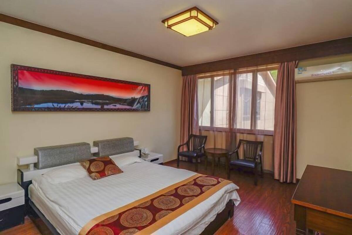 A hotel room with a bed, a desk, a chair, a painting on the wall, and a window with curtains.