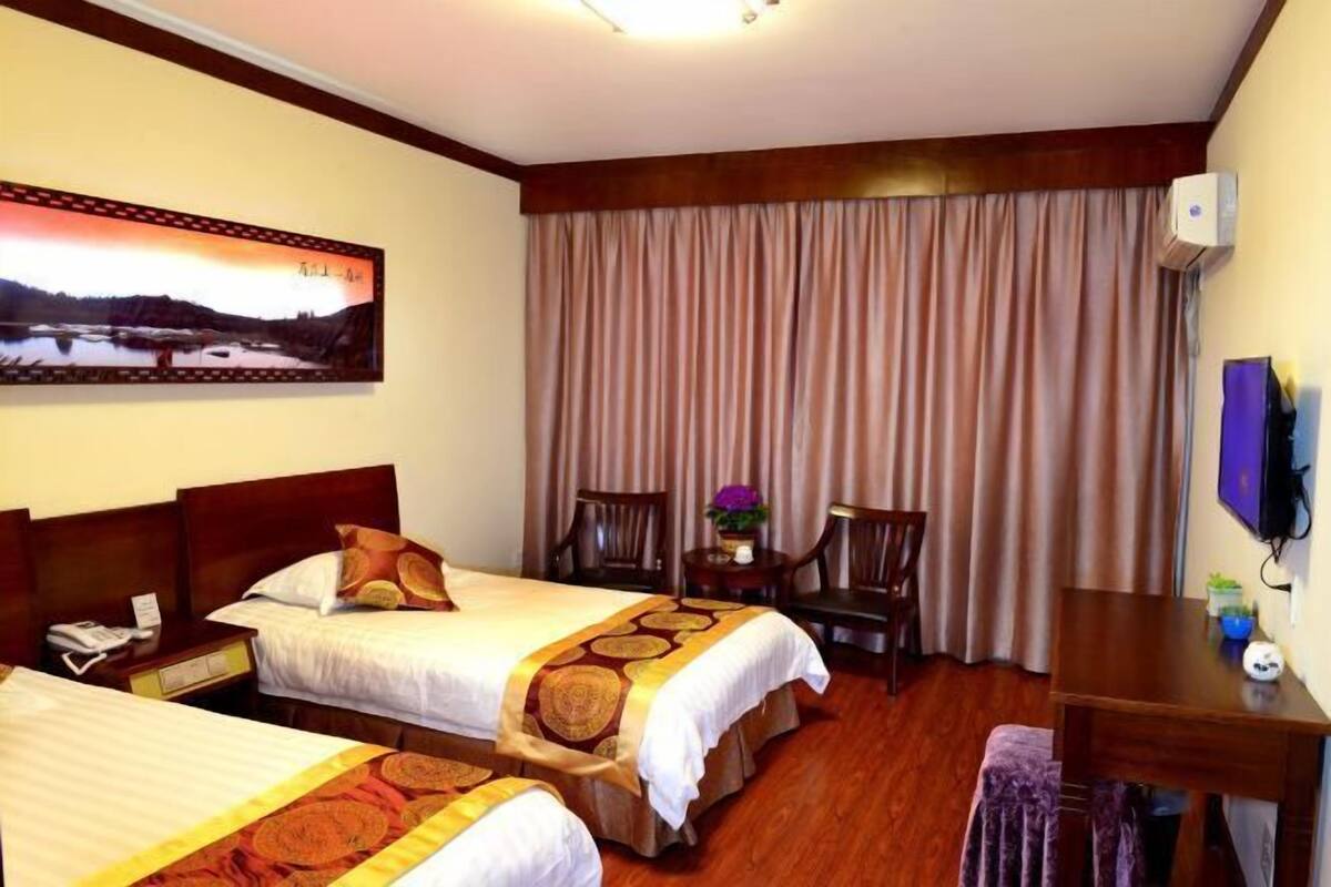 A hotel room with two beds, a desk, a chair, a TV, and a painting on the wall.