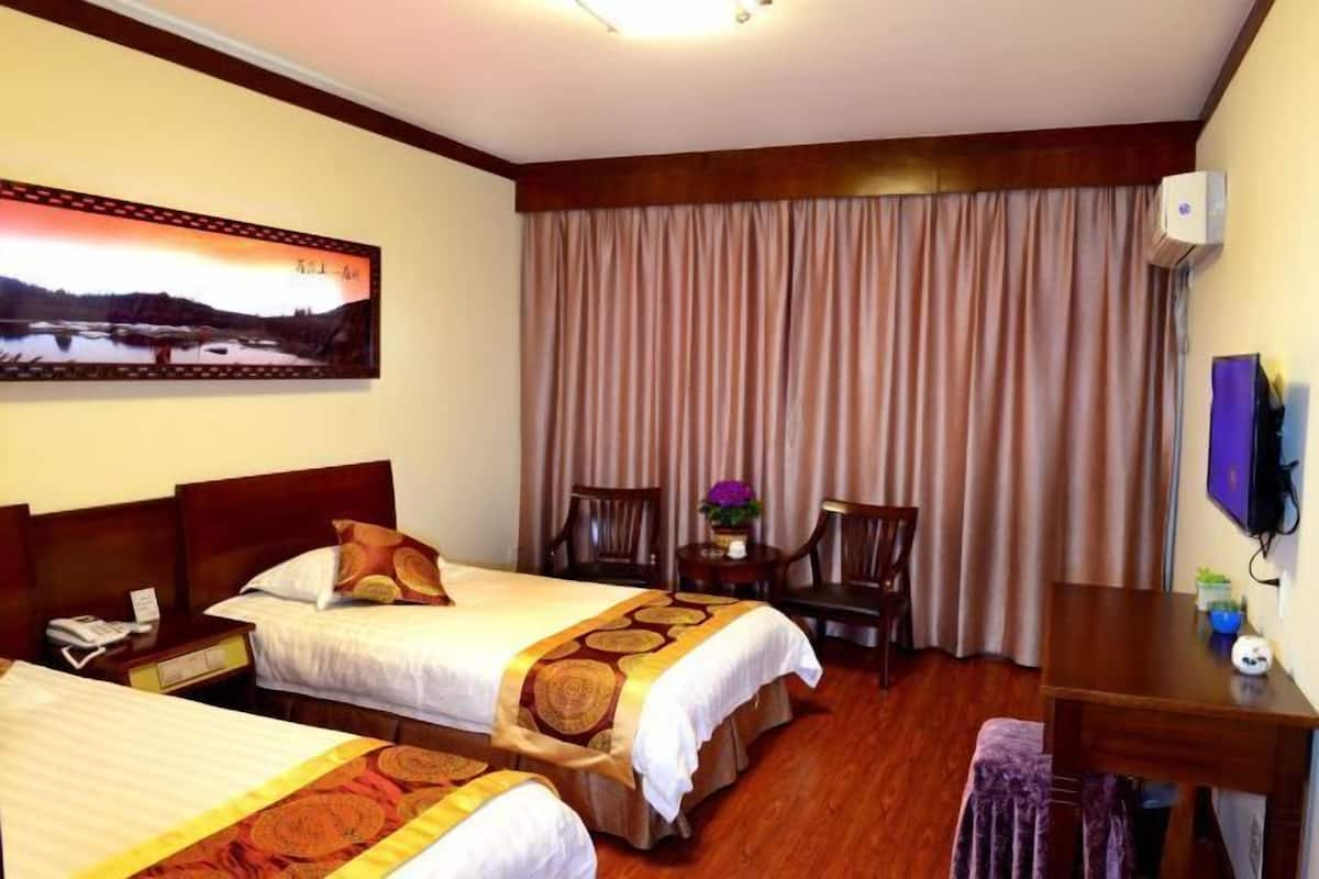 A hotel room with two beds, a desk, a chair, a TV, and a painting on the wall.
