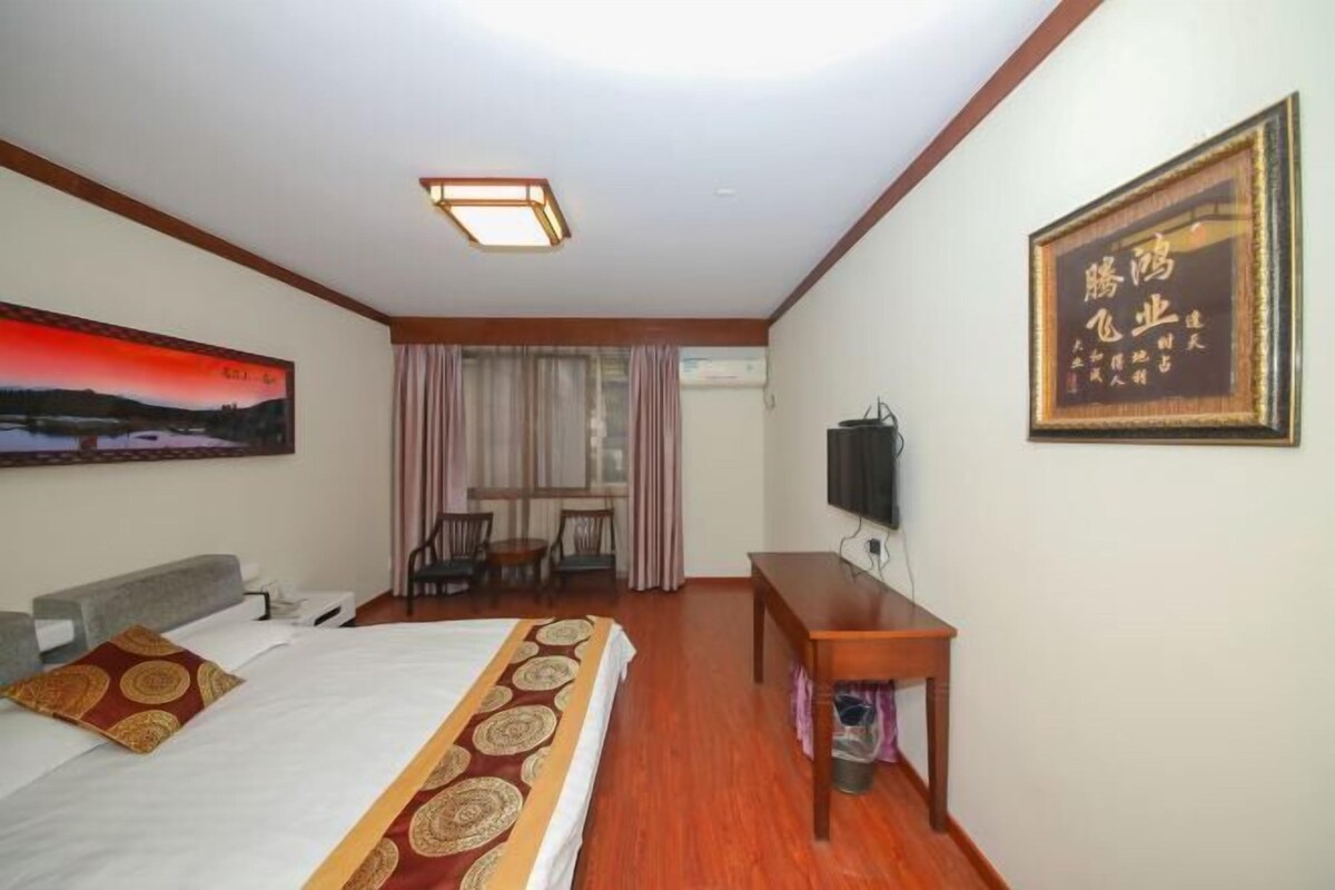 A hotel room with a bed, a desk, a chair, a TV, and a painting on the wall.