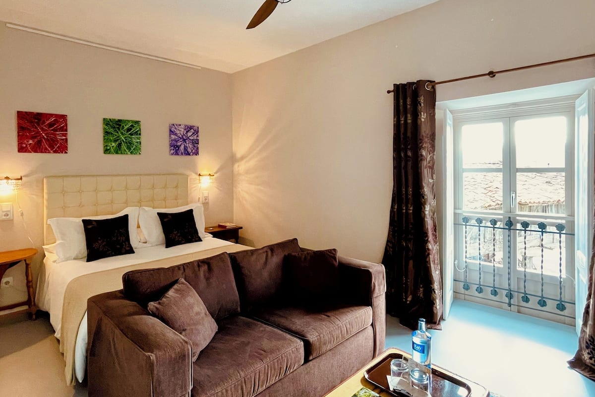 Una habitación de hotel con una cama, un sofá marrón, una ventana con cortinas y decoración en la pared.