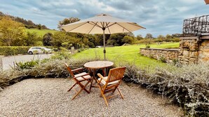 Un patio con una mesa, sillas y una sombrilla, junto a un muro de piedra.