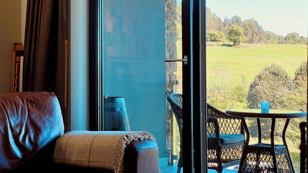 Una habitación con puerta corrediza de vidrio que da a un balcón con vistas a un campo verde y árboles.