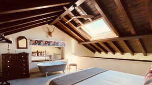 Un dormitorio con techo inclinado, un ventanal grande, una bañera, un aparador y un espejo.