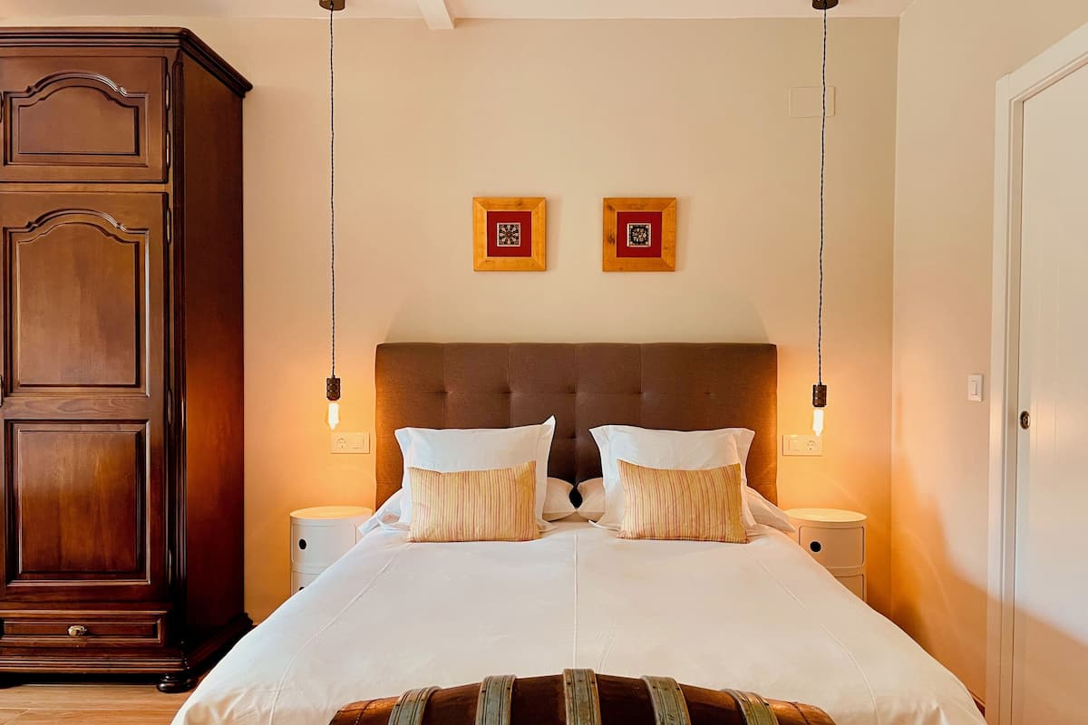 Un dormitorio con una cama grande, dos mesitas de noche, un armario de madera y dos cuadros colgados en la pared.