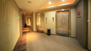 A hotel corridor with carpeted floors, two elevators, and a trash can. - Homeinns Neo Wuhu Wanzhi XinwuDevelopment Zone Hotel (Wuhu)