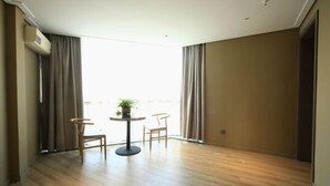 A room with a wooden floor, a round table with chairs, a potted plant, and a window with curtains. - Homeinns Neo Wuhu Wanzhi XinwuDevelopment Zone Hotel (Wuhu)