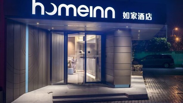 L’entrée d’un hôtel au design moderne, avec une porte en verre et une enseigne portant le nom « homeinn ».