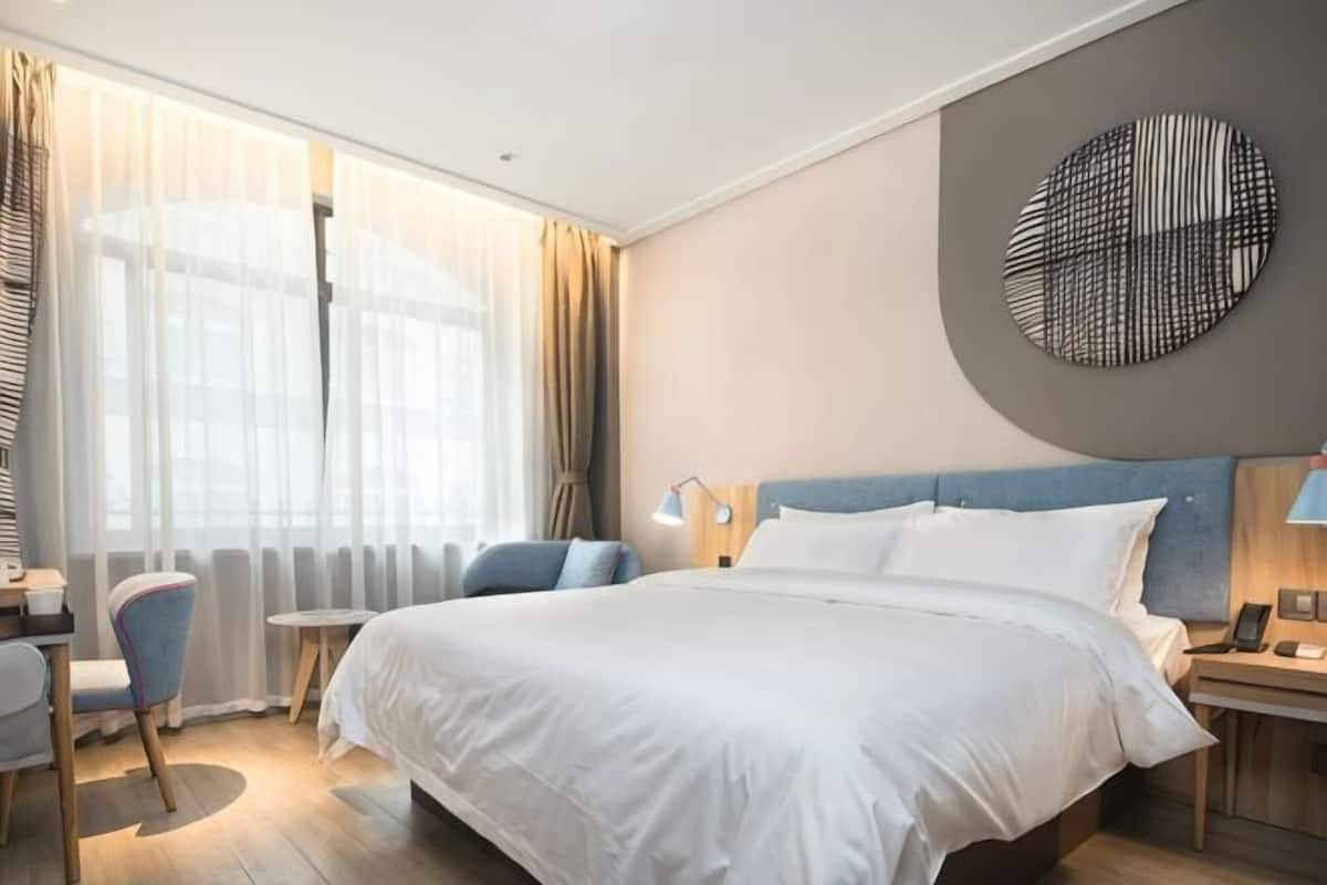 A hotel room with a large bed, a desk, a chair, and a view of the outdoors.