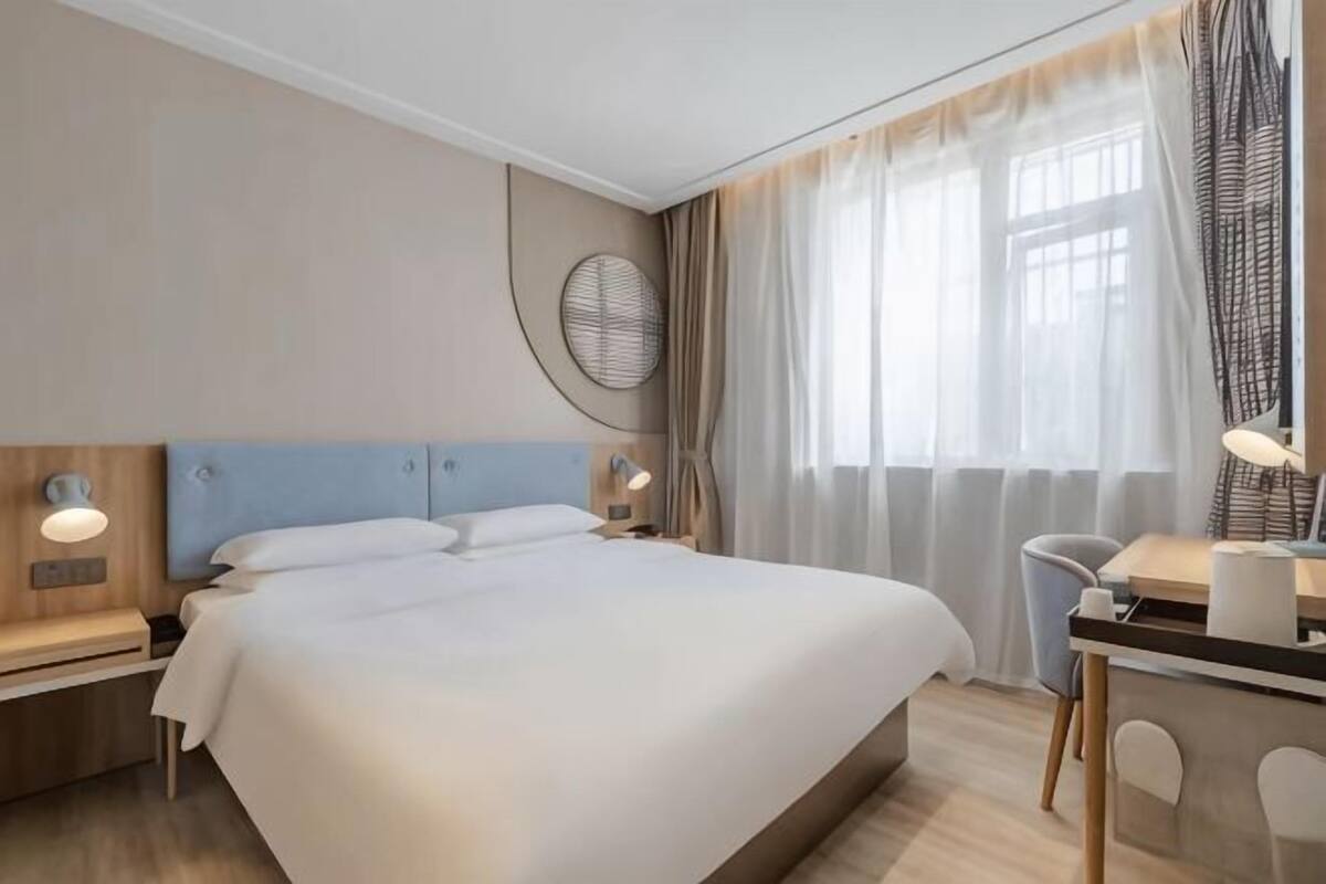 Hotellihuone, jossa on suuri sänky, yöpöydät, työpöytä tuolilla sekä ikkuna, jossa on verhot.