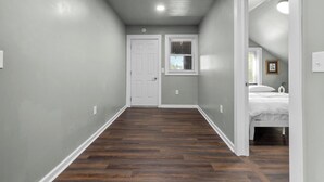 Un pasillo estrecho con paredes grises y suelo de madera que conduce a un dormitorio con cama y ventana.