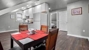 Un comedor con una mesa dispuesta para cuatro, una cocina al fondo y un dormitorio visible a través de una puerta abierta.