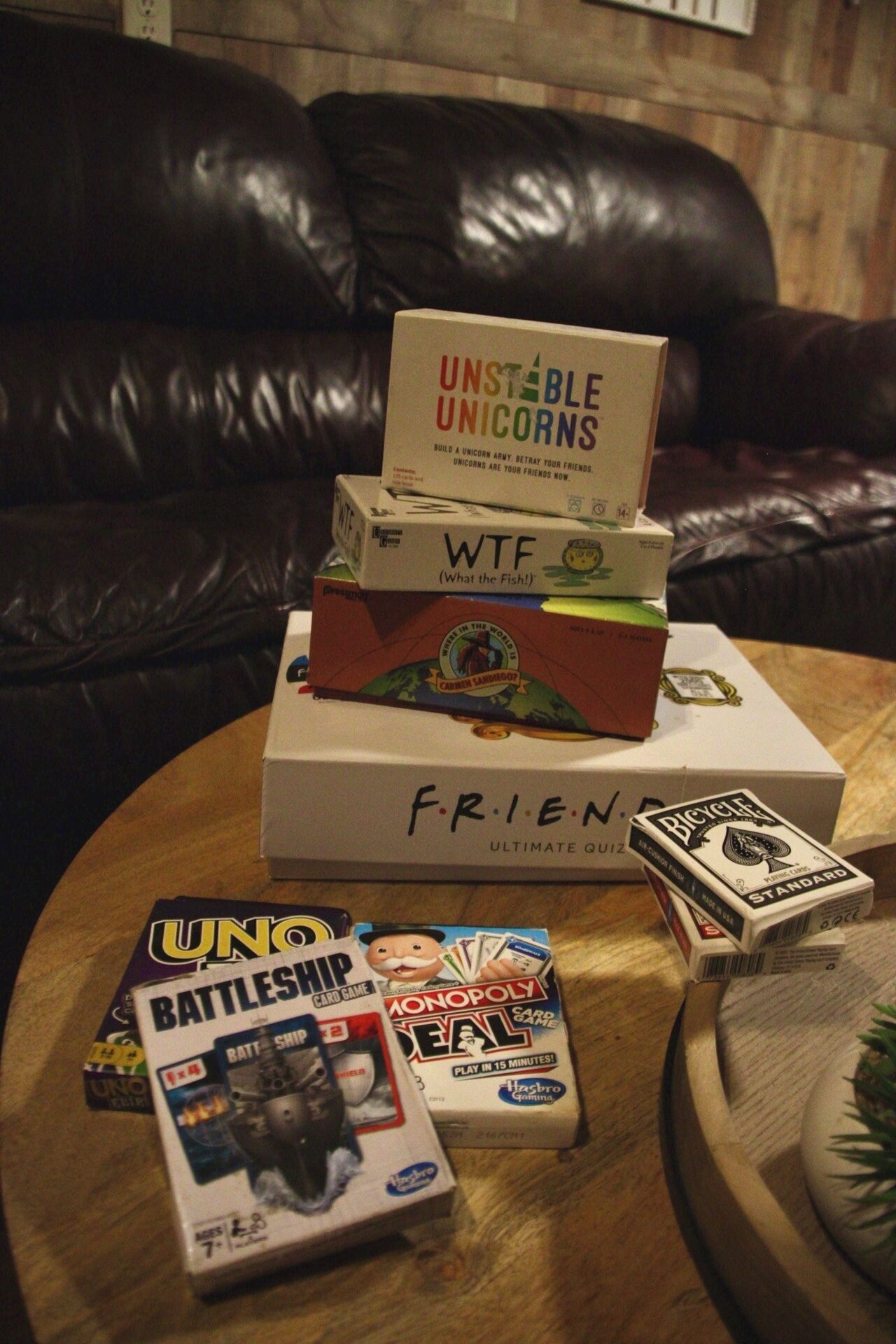 A variety of board games on a wooden table, including 'Battleship', 'Uno', 'Monopoly', 'WTF', and 'Bicycle'.