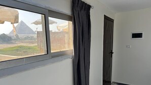 Una habitación con un ventanal grande, una puerta y un pequeño equipo de aire acondicionado en la pared.