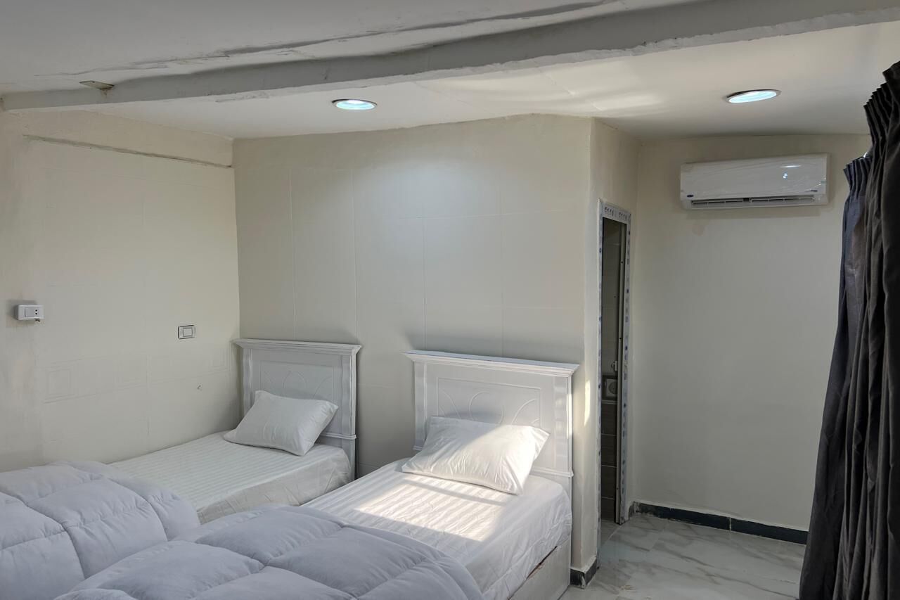 A hotel room with two single beds, a ceiling with recessed lighting, an air conditioning unit, and a door.