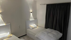 Habitación de hotel con dos camas individuales, una mesita de noche, una lámpara de pared y una ventana con cortinas.