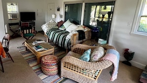 Een gezellige woonkamer met een bank, een salontafel en een rieten fauteuil. Er staat een televisie en een lamp in de kamer.