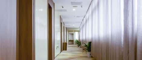 A hotel corridor with a patterned carpet, wooden doors, and a long row of curtains on one side.