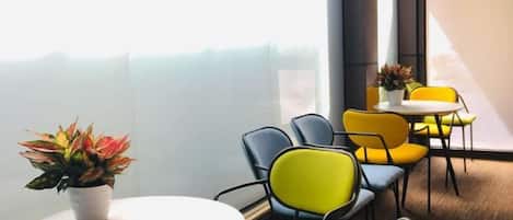 A modern interior with round tables and chairs, a potted plant, and a view through a glass partition.