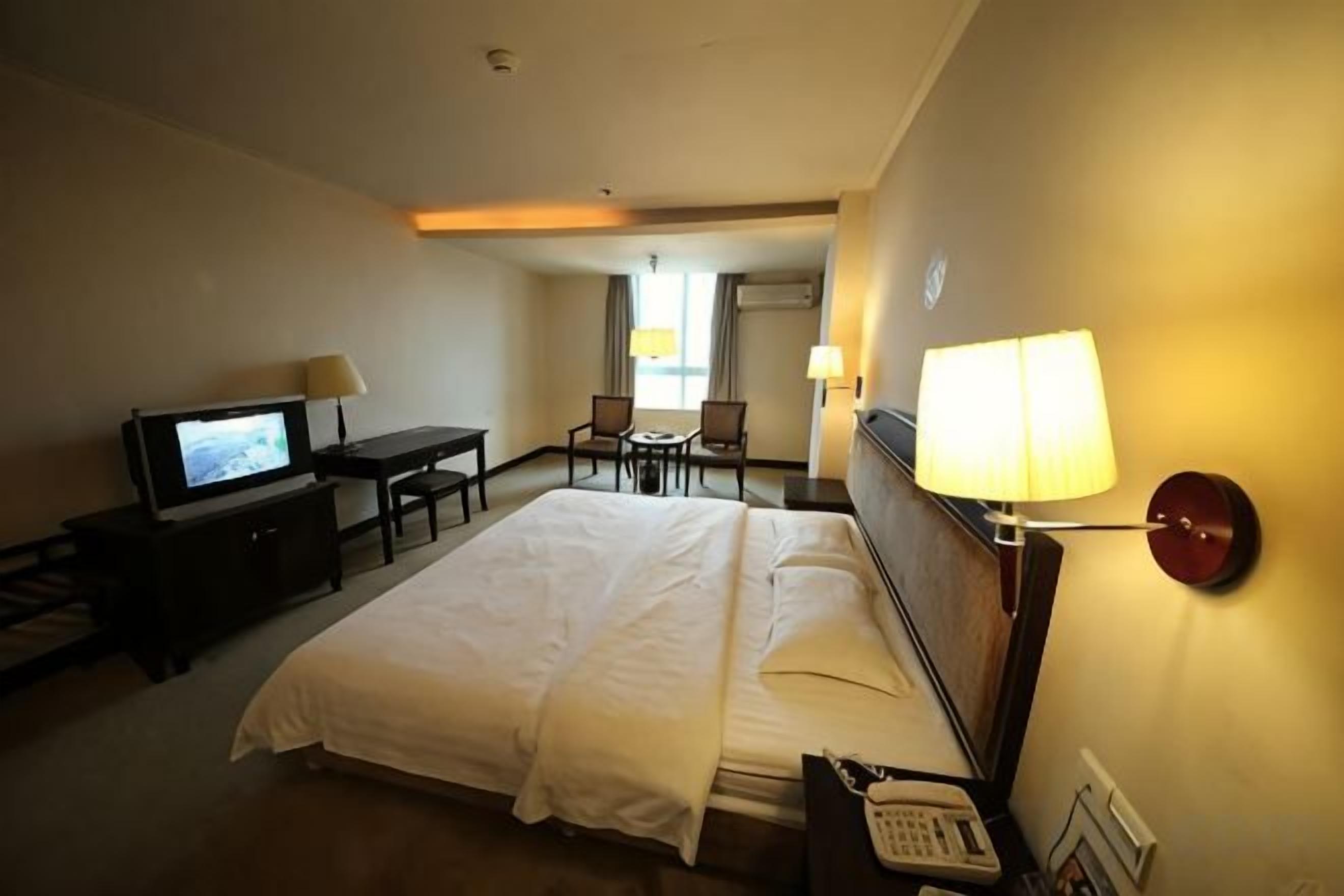 A hotel room with a bed, a desk, a television, and a lamp.