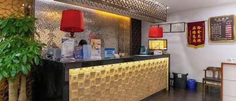 A reception desk with a patterned backdrop, a potted plant, and a red lamp.