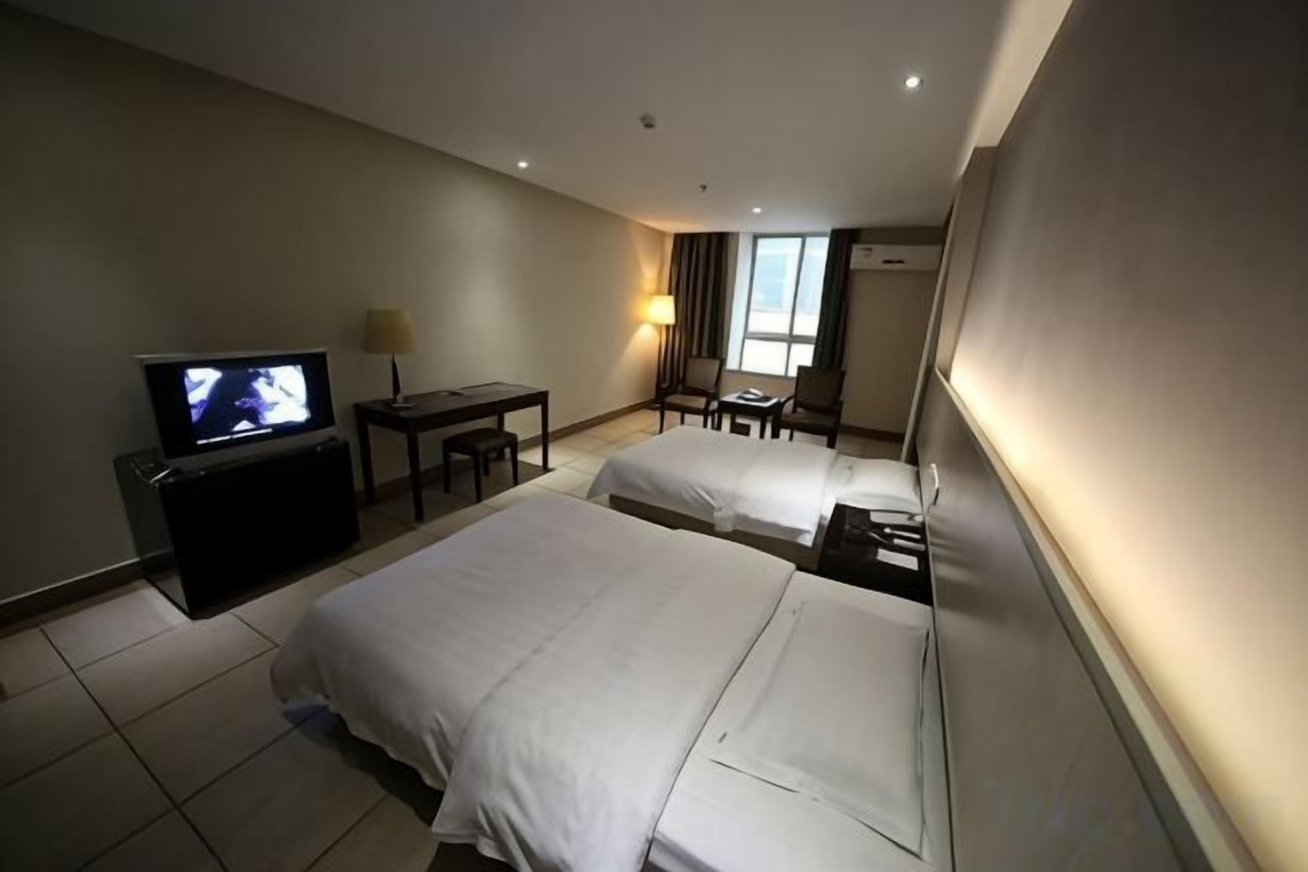 Habitación de hotel con dos camas, televisión, escritorio y una silla.