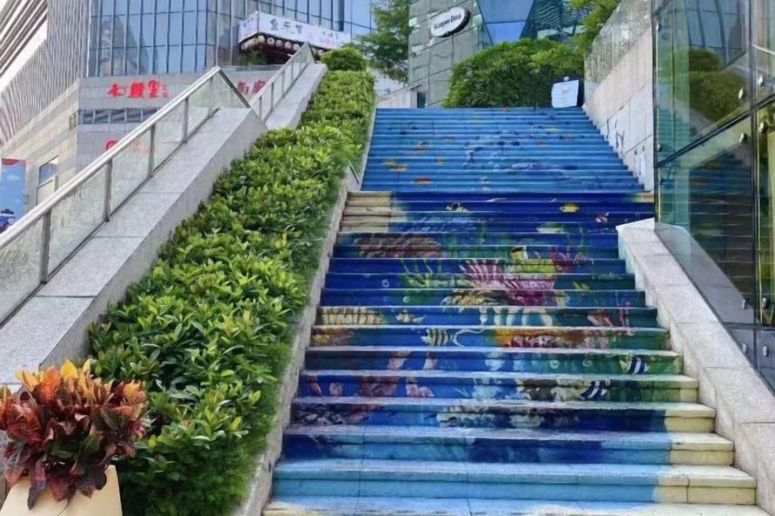 Un escalier orné d’une fresque colorée, entouré de verdure et de bâtiments modernes.